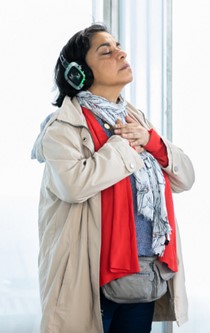 Beschrijving afbeelding: rechtstaande dame met gekruiste handen op de borst, gesloten ogen. Zij draagt een headset en is geconcentreerd aan het luisteren.