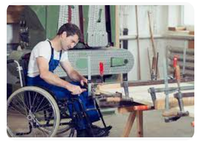 Beschrijving afbeelding: jongeman, rolstoelgebruiker, in werkkledij, is aan het werk in een atelier, verschillende machines op de achtergrond.